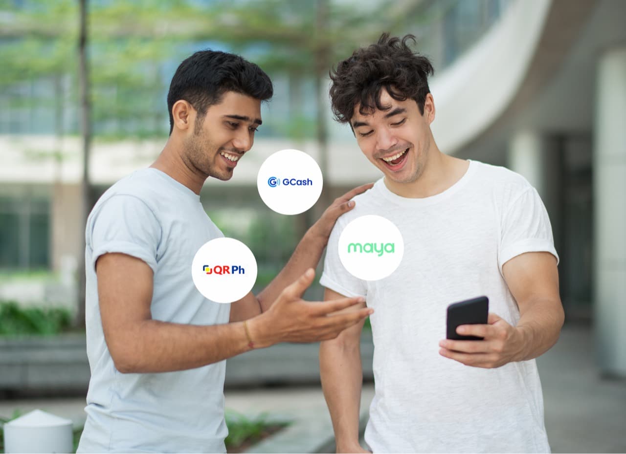 Two friends smiling at a phone, ringed by GCash, Maya, and QRPH payment badges